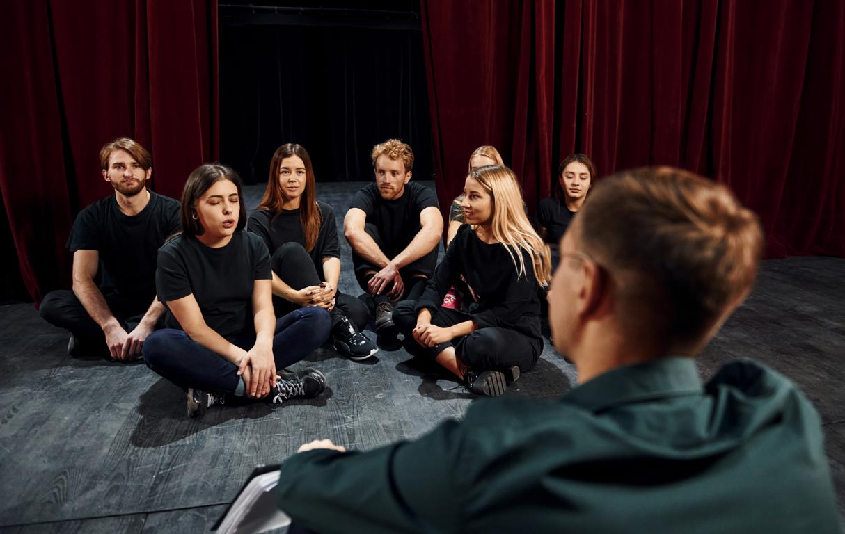 Jugendliche sitzen für Schauspielkurse in der Gruppe auf der Bühne